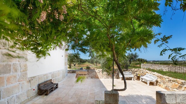 Un patio de piedra con mobiliario exterior y vistas a un muro de piedra y follaje.