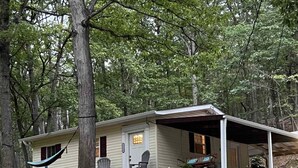 Eine Hütte mit Veranda, einer Hängematte und einem kleinen Tisch mit Stühlen.