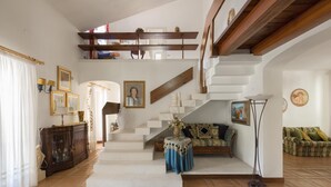 Uma sala de estar ampla com escada para um andar superior, um conjunto de sofás e uma mesa decorativa.