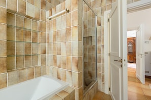A bathroom with a white bathtub, glass shelves, and a shower area with a glass door.