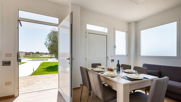 Ein moderner Essbereich mit einem Tisch für vier Personen, großen Fenstern und Blick auf eine angelegte Außenanlage.