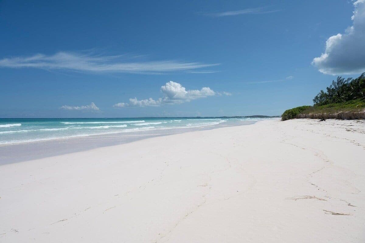 A wide, white sandy beach with gentle waves and a clear blue sky.