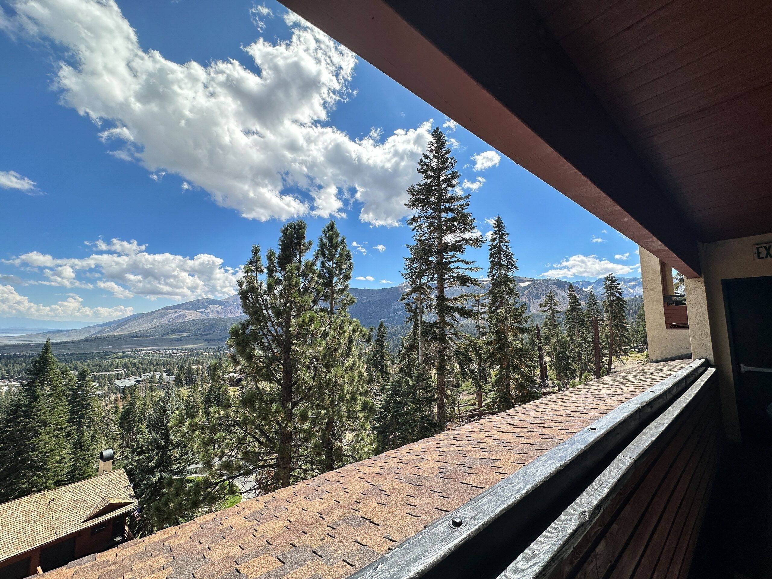 Un balcon donnant sur un paysage montagneux, une terrasse en bois et un bâtiment sur lequel on peut lire l’inscription « EX ».