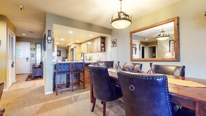 A dining area with a wooden table and black leather chairs, a chandelier, and a large mirror on the wall. - Bridges #108 2 Bedroom Condo by RedAwning (Mammoth Lakes)