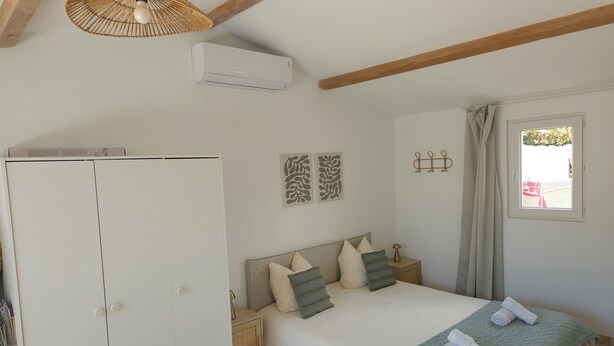 A bedroom with a bed, a wardrobe, a bedside table, a hanging light fixture, and a window with curtains. - Gîte des Baumes (Beaumettes)