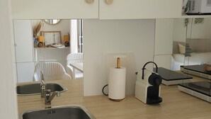 A compact kitchen with a built-in washing machine, a sink, and a countertop with a paper towel dispenser and a coffee machine. - Gîte des Baumes (Beaumettes)