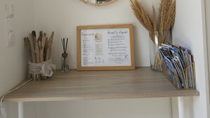 A room with a wooden shelf displaying a welcome sign, a round mirror, and decorative items including dried plants and magazines. - Gîte des Baumes (Beaumettes)