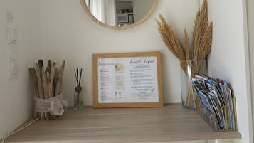 Une pièce avec une étagère en bois où sont exposés un panneau d’accueil, un miroir rond et des objets décoratifs, notamment des plantes séchées et des magazines.