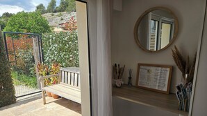 A room with a wooden bench, a mirror, a welcome sign, and a shelf with magazines and reed sticks. - Gîte des Baumes (Beaumettes)