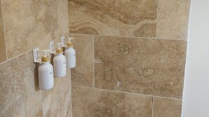 A bathroom with beige tiles and three white bottles mounted on the wall. - Gîte des Baumes (Beaumettes)