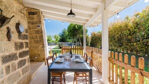 An outdoor patio with a table set for dining, stone walls, and a wooden fence. - 3625 Villa Queen by Perle di Puglia (Lecce)