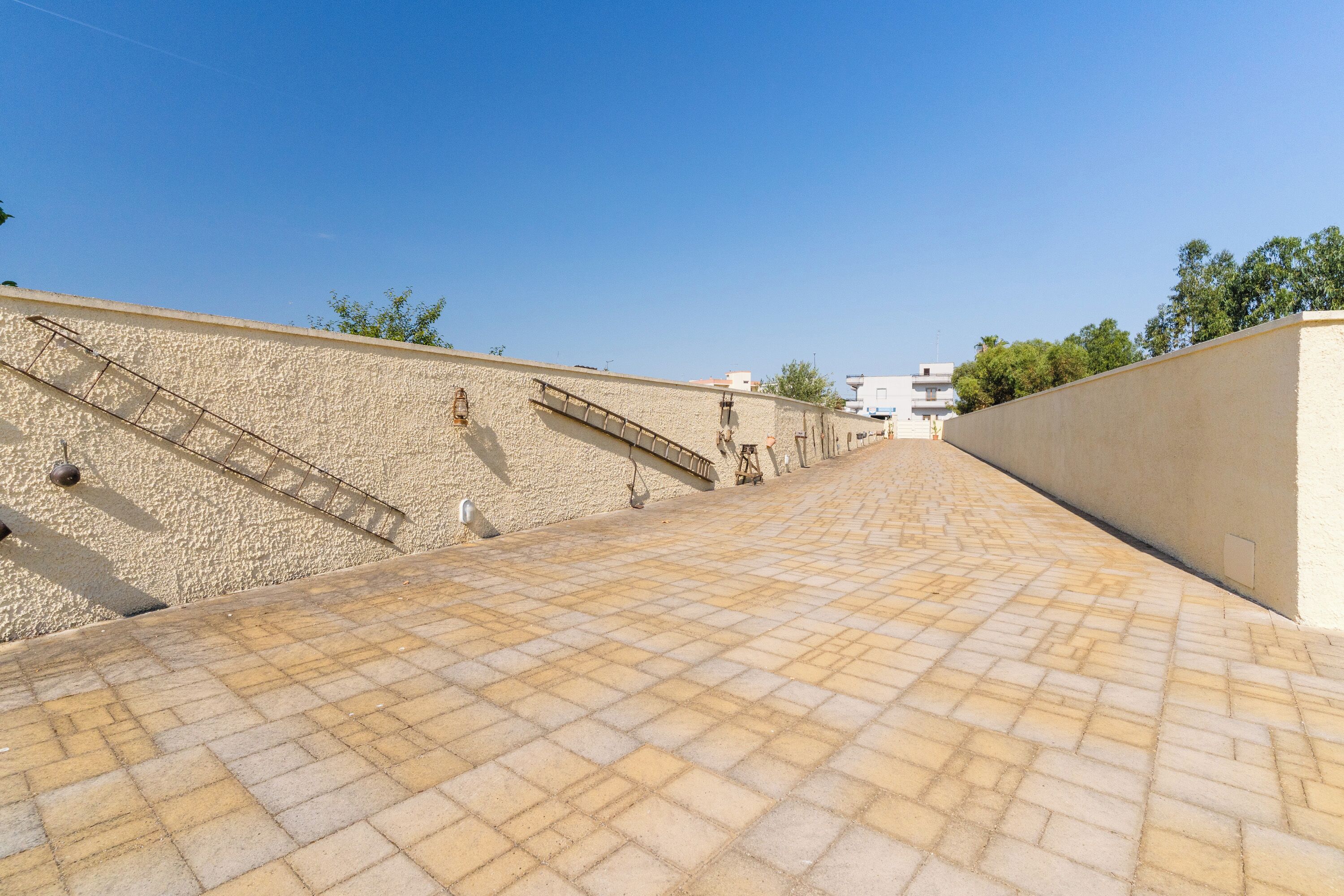 Un sendero pavimentado que conduce a un edificio con un muro texturizado y una escalera de metal.