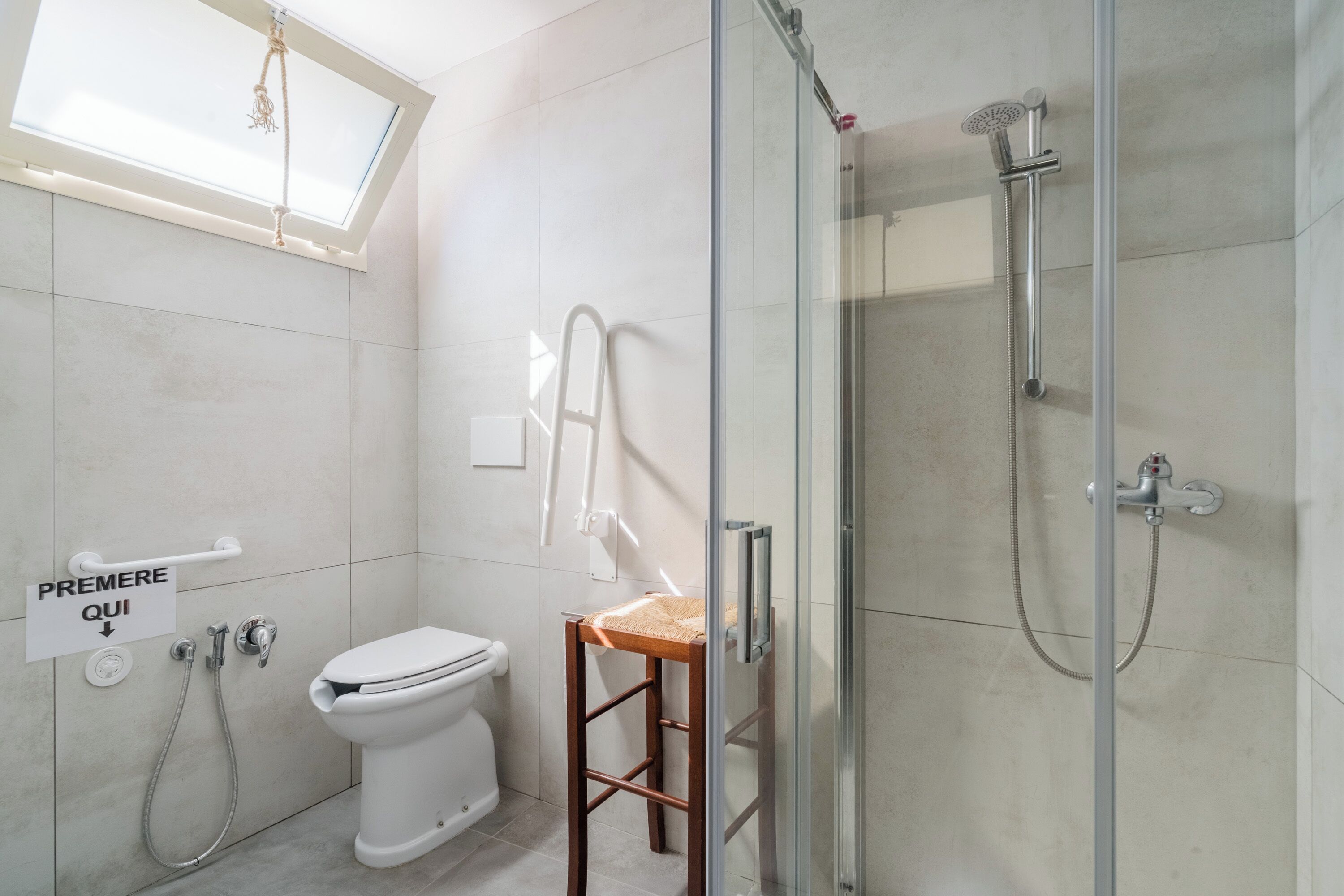 A bathroom with a toilet, a shower, a glass-enclosed shower area, a wooden stool, and a skylight.