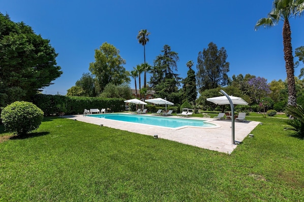 A swimming pool with lounge chairs and umbrellas, surrounded by well-maintained grass and trees.