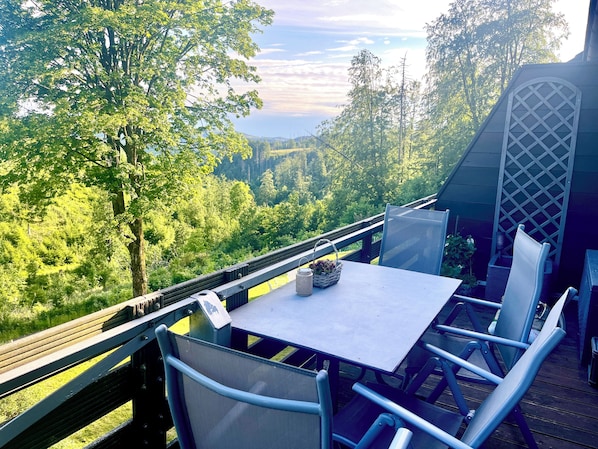 Terraza al aire libre con mesa y sillas, con vista a un área boscosa.