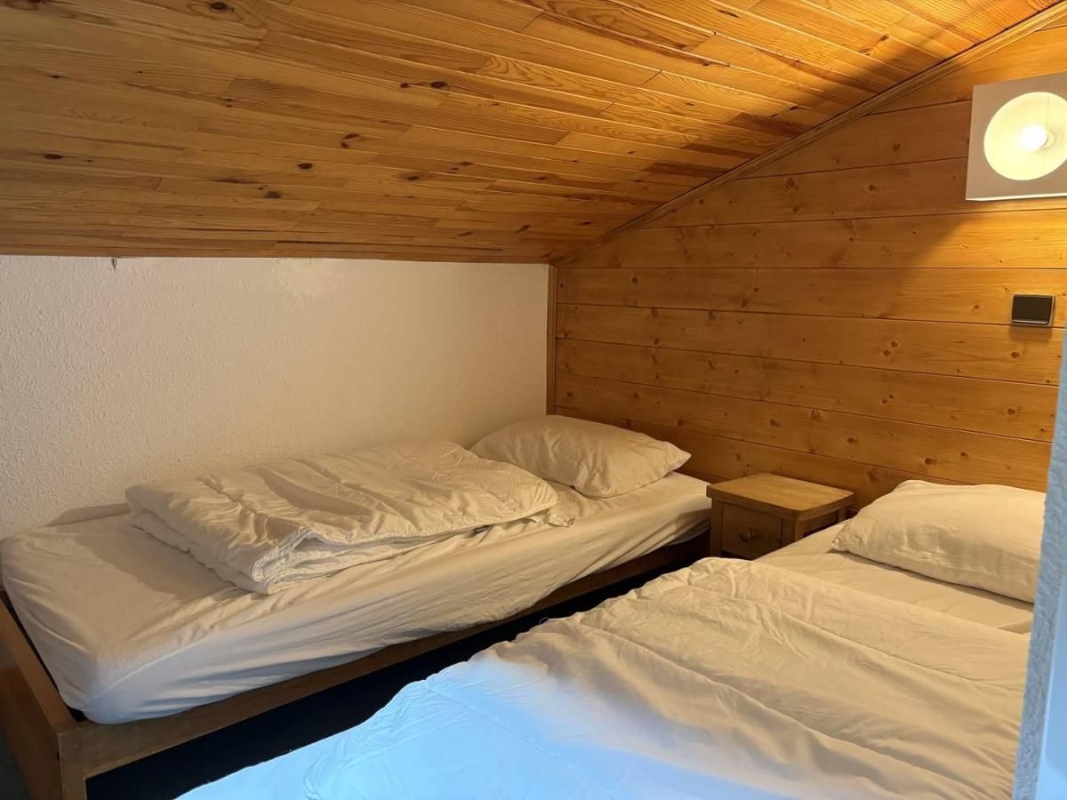 A small, single-room cabin with a wooden ceiling and walls, a bunk bed, a bedside table, and a wall-mounted light fixture.
