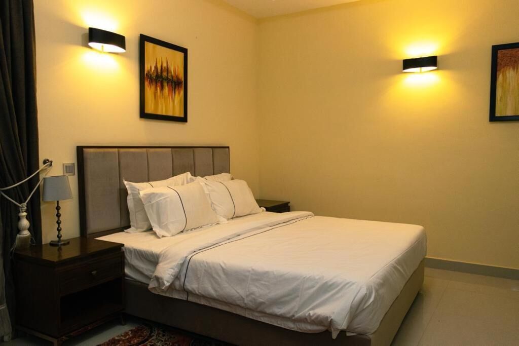 A neatly made bed with white linens, a bedside table with a lamp, and two wall-mounted light fixtures.