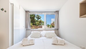 A neatly made bed with white linens and towels, a large window with curtains, and a view of greenery outside. - 3514 Mareo Apartment by Barbarhouse (Polignano a Mare)