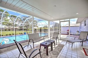 A covered outdoor area with a pool, chairs, and a table.