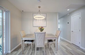 A dining area with a table, four chairs, a chandelier, and a framed artwork above the table.