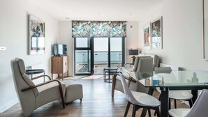Uma sala de estar moderna com mesa de vidro, assentos confortáveis, vista para o mar e obras de arte nas paredes.