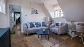 A modern loft apartment with a loft bed, a grey sofa set, a round coffee table, and a dining area with a wooden chair and table.