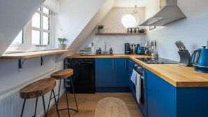 A kitchen with blue cabinets, a wooden countertop, a dishwasher, a coffee machine, and a hanging light fixture.