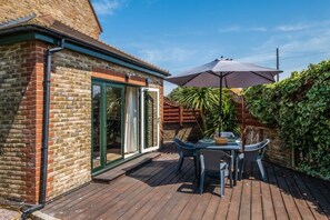 Une terrasse avec une table et des chaises, une porte-fenêtre coulissante et un grand parasol.