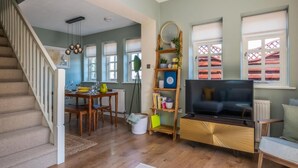 A living room with a staircase, a dining area, and a TV on a wooden cabinet. - Garden apartment with parking in Rye (Rye)