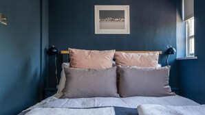 A neatly made bed with a wooden headboard, two bedside lamps, and a framed picture on the wall. - Garden apartment with parking in Rye (Rye)