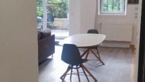 Un intérieur moderne avec un coin repas comprenant une table ronde et des chaises, un canapé et une vue sur l’extérieur grâce à de grandes fenêtres.