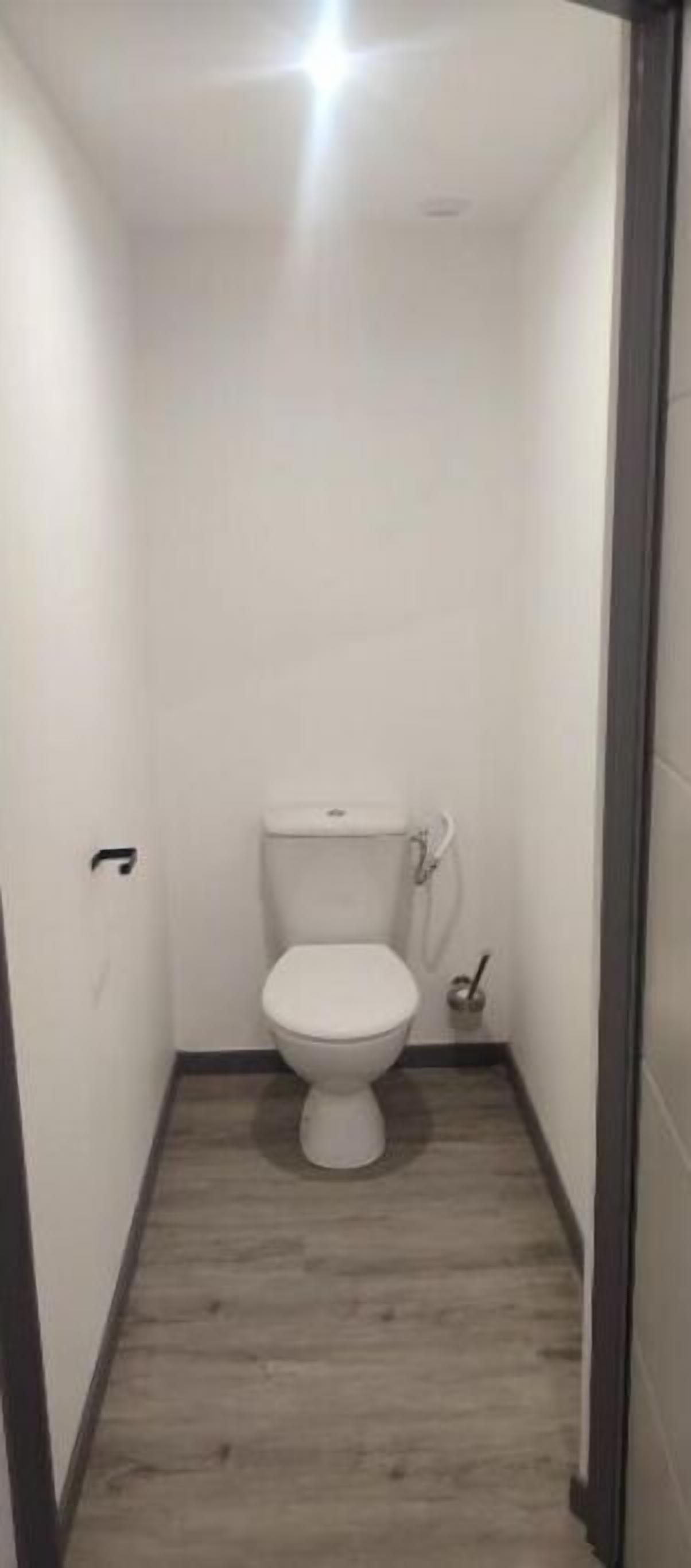 Un baño pequeño y estrecho con un inodoro blanco, suelo de madera y pared blanca.