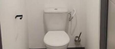 Un baño pequeño y estrecho con un inodoro blanco, suelo de madera y pared blanca.