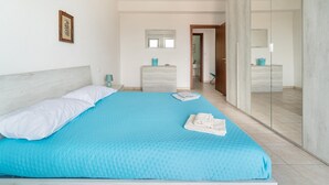 Une chambre à coucher avec un grand lit, une commode, un miroir et une porte donnant sur une autre pièce.