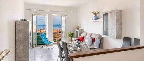A modern living room with a dining area, large windows, and a view of the sea.