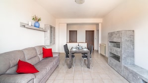 Un salon moderne avec un canapé gris, des coussins rouges, une table à manger avec des chaises et un meuble gris.