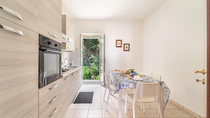 Une cuisine moderne dotée d’un four et d’un micro-ondes encastrés, un coin repas avec une table et des chaises, et une vue sur un jardin par une porte ouverte.