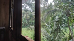 A view from a window with a wooden frame and a small table, overlooking a lush garden with palm trees and other greenery. - Green Herbal Ayurvedic Eco-Chalets  (Unawatuna)