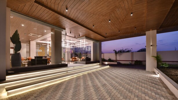 A modern building with a brick-paved outdoor area, wooden ceiling, and illuminated steps leading to a glass entrance. - Click Hotel Pithampur (Dr. Ambedkar Nagar)