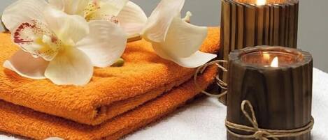 A stack of orange towels, a lit candle, and a white orchid.