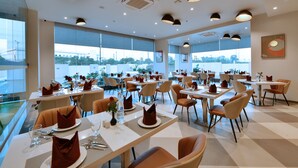 A modern dining area with tables set for service, large windows offering views of the city, and a clean, contemporary interior design. - Click Hotel Pithampur (Dr. Ambedkar Nagar)