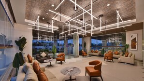 A modern lounge area with sofas, armchairs, and a coffee table, featuring a brick ceiling and large windows with a city view. - Click Hotel Pithampur (Dr. Ambedkar Nagar)