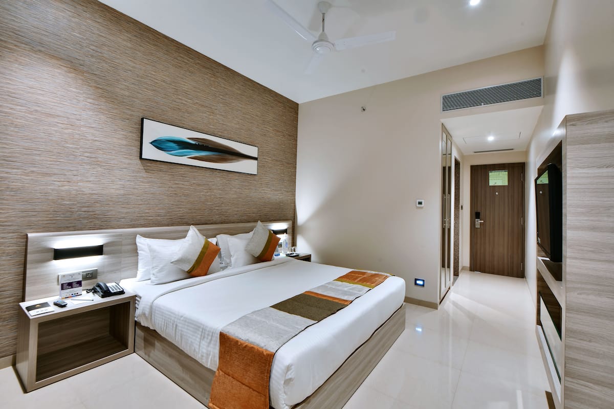 A modern hotel room with a large bed, a bedside table with a phone and charger, a wall-mounted artwork, and a ceiling fan.