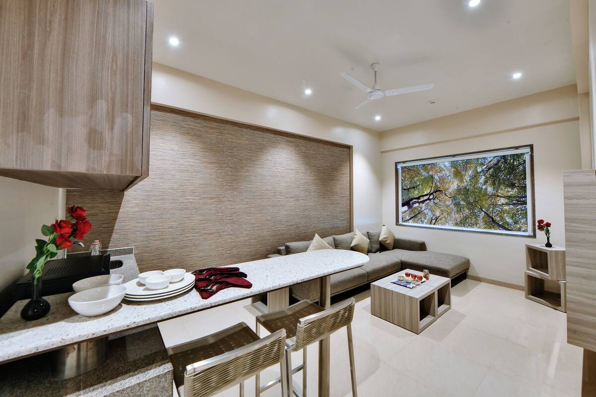 A modern kitchen with a dining area, a large window with a tree view, and a ceiling fan.