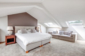 Une chambre avec un grand lit, un canapé, une table de chevet et une lucarne.