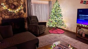 A cozy living room with a stone wall, a fireplace, a Christmas tree, and a television displaying a message. - Let our place be the basecamp for your exploration at Yosemite! (Mariposa)