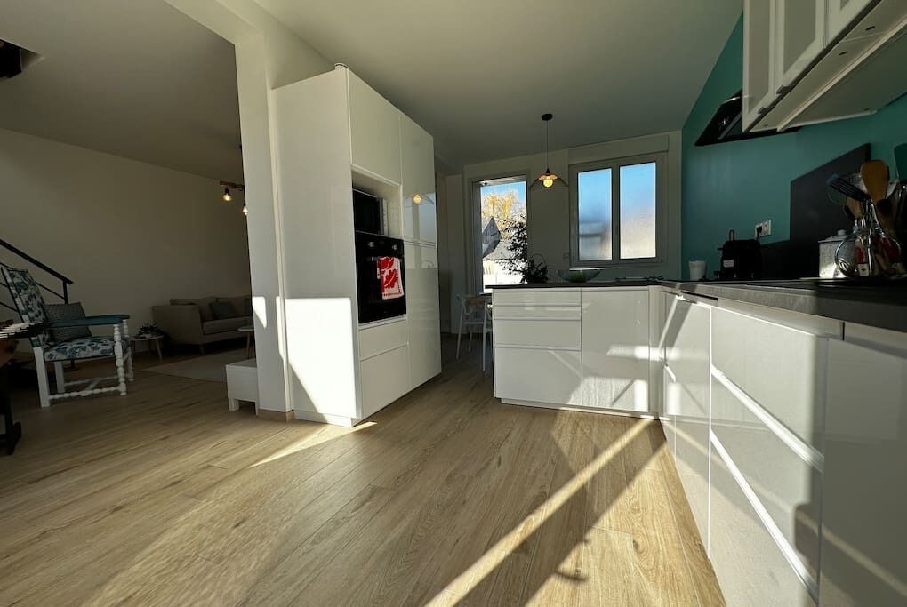 Een moderne keuken met witte kasten, een centraal eiland en een eetgedeelte met tafel en stoelen.