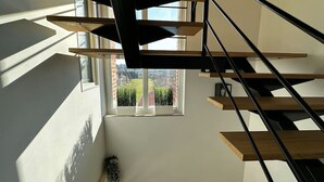 Una escala moderna amb graons de fusta i baranes metàl·liques, que condueix a una finestra amb vista a un jardí.