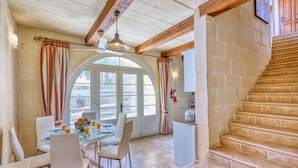 A dining area with a glass table, white chairs, and a fruit bowl. There is a staircase leading to an upper level. - Karmnu - Ghasri Holiday Home (L-Għasri)