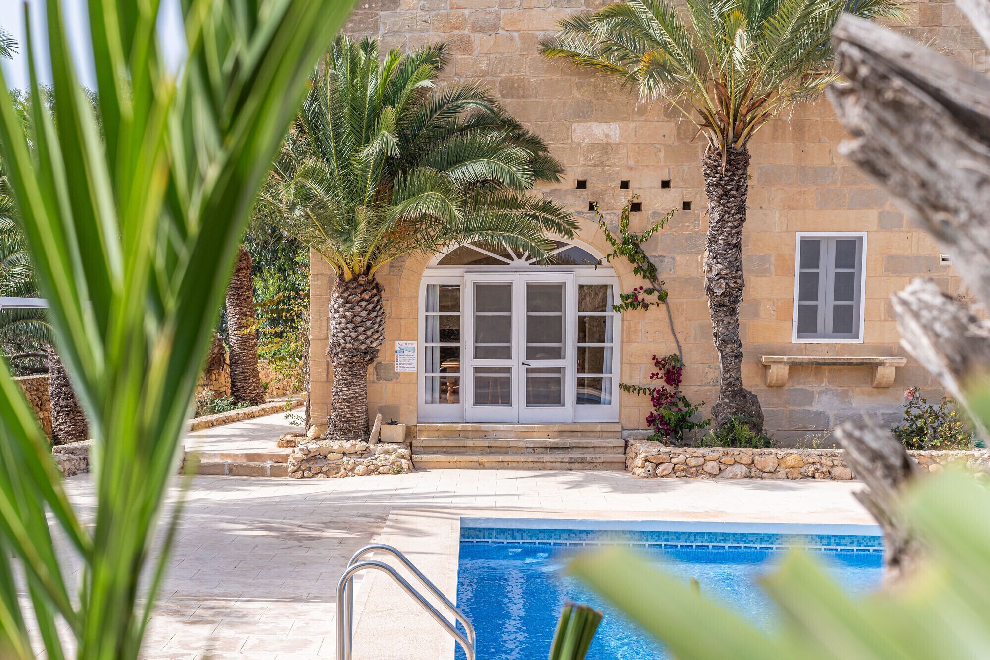 A pool area with a stone building, palm trees, and a clear blue pool.